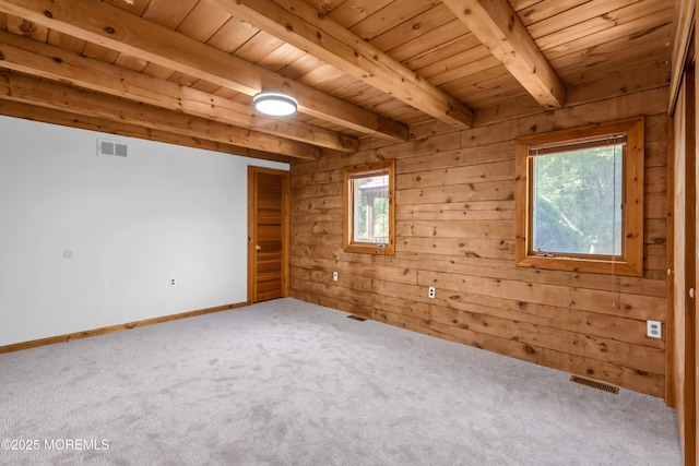 carpeted empty room with wood walls, beamed ceiling, and wooden ceiling