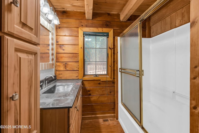 bathroom featuring beam ceiling, shower / bath combination with glass door, wooden walls, and vanity