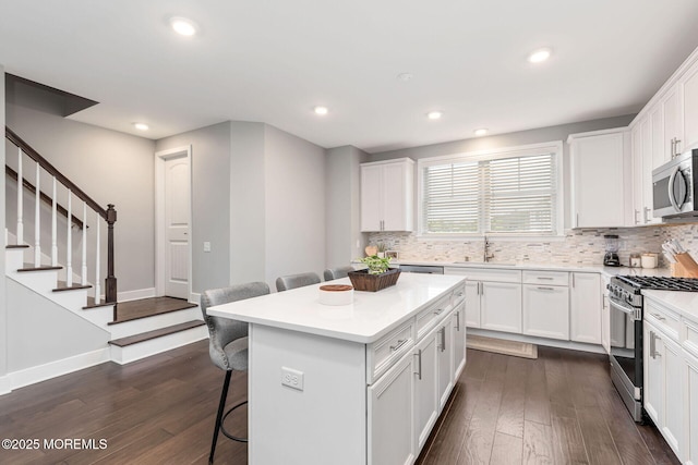 kitchen featuring a breakfast bar area, stainless steel appliances, dark wood-style flooring, a sink, and white cabinets