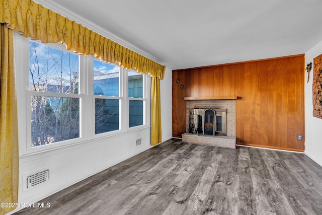 unfurnished living room featuring wood-type flooring, a brick fireplace, and wood walls