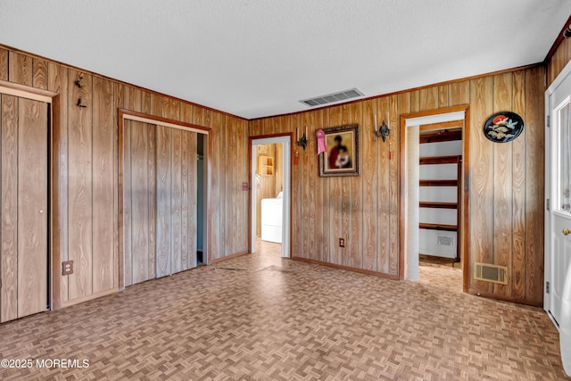 unfurnished bedroom featuring a textured ceiling, light parquet flooring, washer / dryer, and wood walls