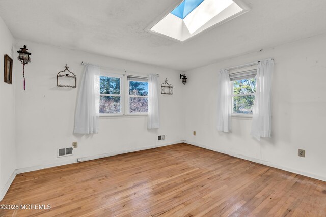 empty room with light wood-type flooring and a skylight