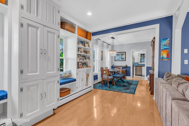 interior space featuring baseboard heating, built in features, crown molding, and light wood-type flooring