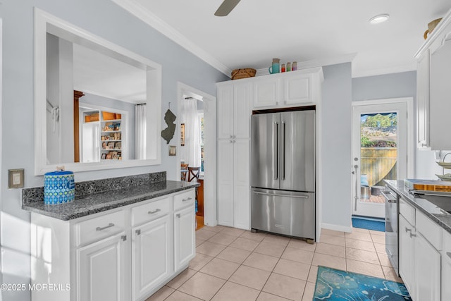 kitchen featuring white cabinets, stainless steel appliances, dark stone countertops, ornamental molding, and light tile patterned floors