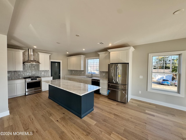 kitchen with sink, wall chimney exhaust hood, stainless steel appliances, a kitchen island, and white cabinets