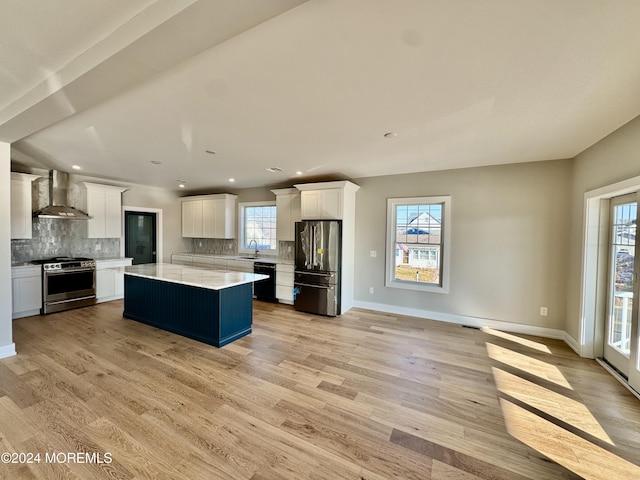 kitchen featuring white cabinetry, wall chimney exhaust hood, stainless steel appliances, and a kitchen island