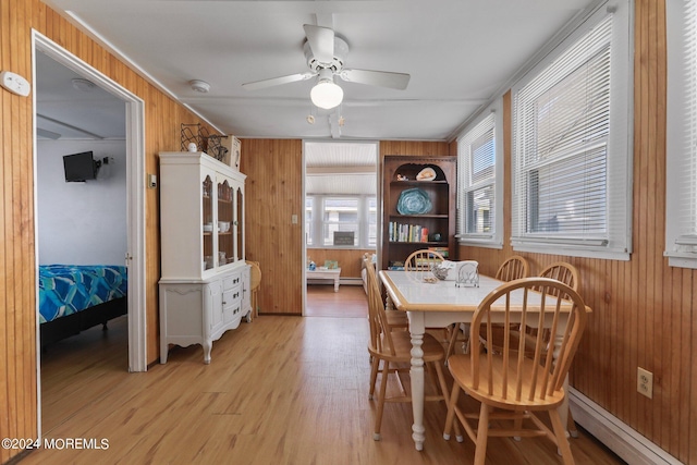 dining space with ceiling fan, wood walls, light hardwood / wood-style flooring, and a baseboard heating unit