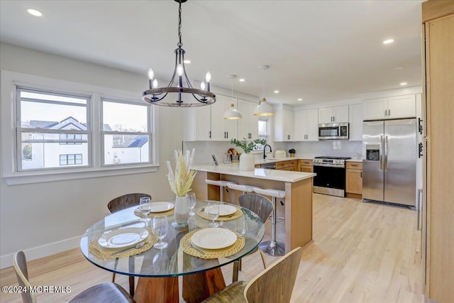 dining space with light wood-type flooring, a notable chandelier, and sink