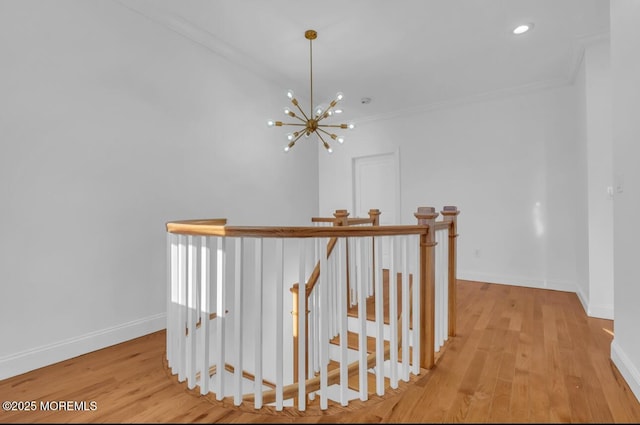 corridor featuring a notable chandelier, ornamental molding, and light wood-type flooring