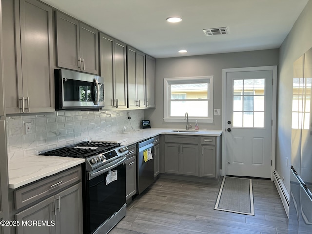 kitchen featuring sink, stainless steel appliances, a baseboard heating unit, gray cabinets, and decorative backsplash