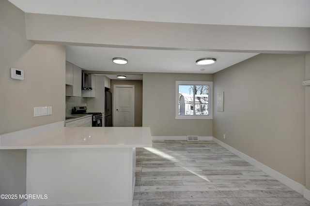 kitchen with kitchen peninsula, decorative backsplash, stainless steel appliances, and light hardwood / wood-style flooring