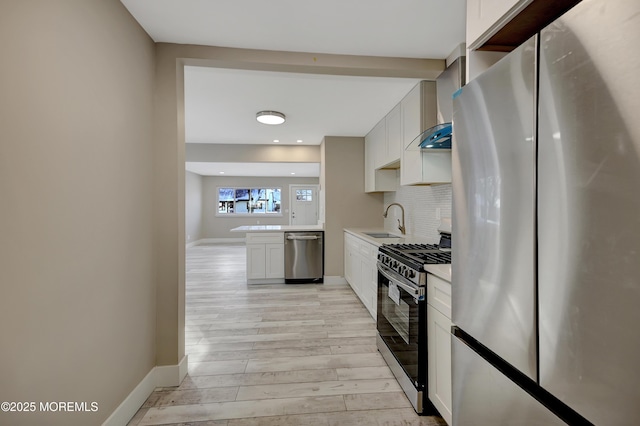 kitchen featuring white cabinets, wall chimney range hood, sink, decorative backsplash, and stainless steel appliances