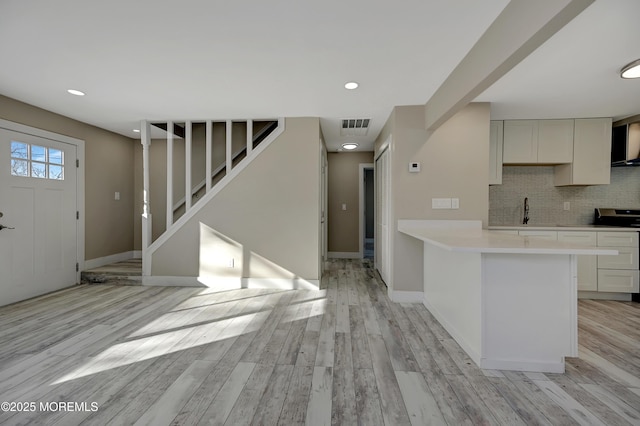 kitchen featuring sink, tasteful backsplash, kitchen peninsula, stove, and light hardwood / wood-style floors