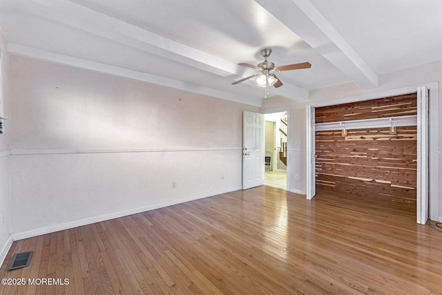 unfurnished bedroom with ceiling fan, beam ceiling, hardwood / wood-style floors, a closet, and wood walls