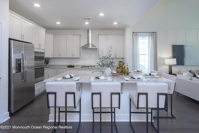 kitchen featuring white cabinetry, a center island with sink, stainless steel appliances, and wall chimney range hood