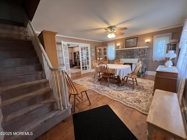 dining space with french doors, hardwood / wood-style flooring, ceiling fan, ornamental molding, and a fireplace