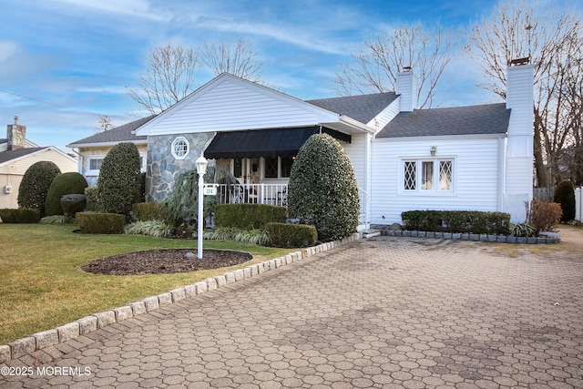 view of front of house featuring a front yard, roof with shingles, a porch, a chimney, and stone siding