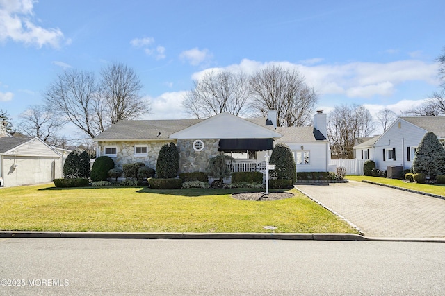 view of front of house featuring fence, a front yard, a chimney, decorative driveway, and stone siding