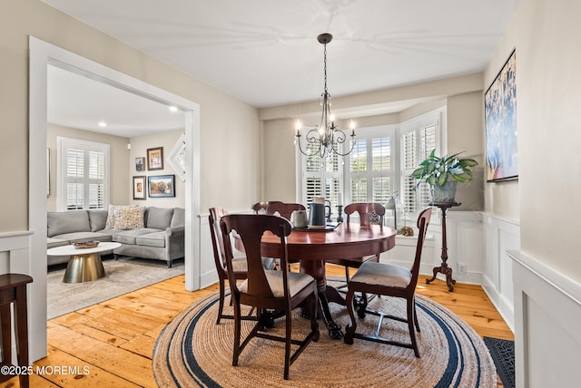 dining area with wainscoting, a notable chandelier, light wood-style flooring, and a decorative wall