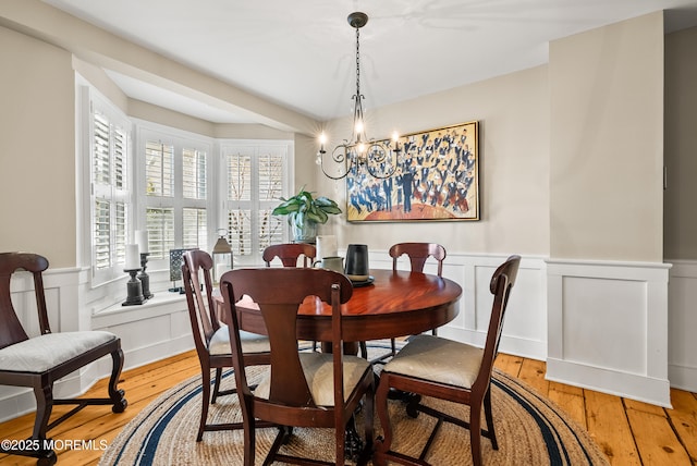 dining space featuring a chandelier, wood-type flooring, and a wainscoted wall