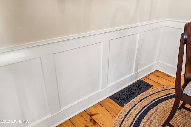 room details with visible vents, a decorative wall, wood finished floors, and wainscoting