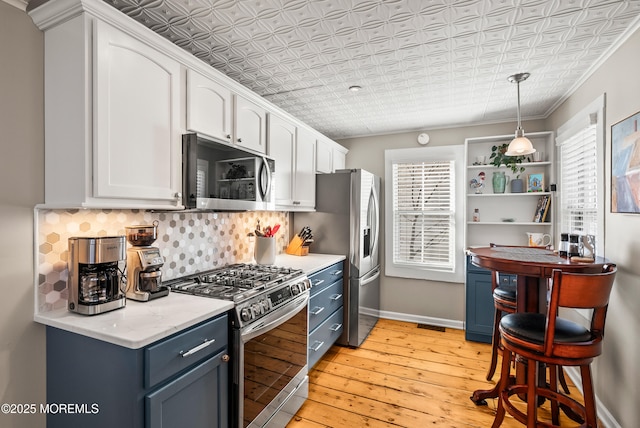 kitchen with appliances with stainless steel finishes, light wood-style flooring, an ornate ceiling, and tasteful backsplash