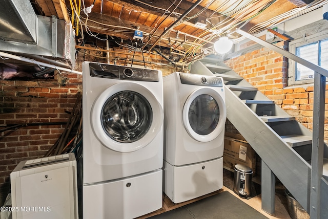 laundry room with laundry area, brick wall, and washer and clothes dryer