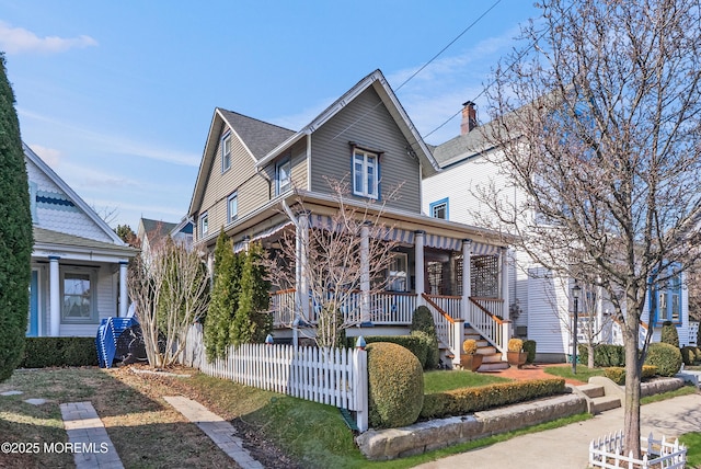 view of front of home with covered porch, a shingled roof, and a fenced front yard