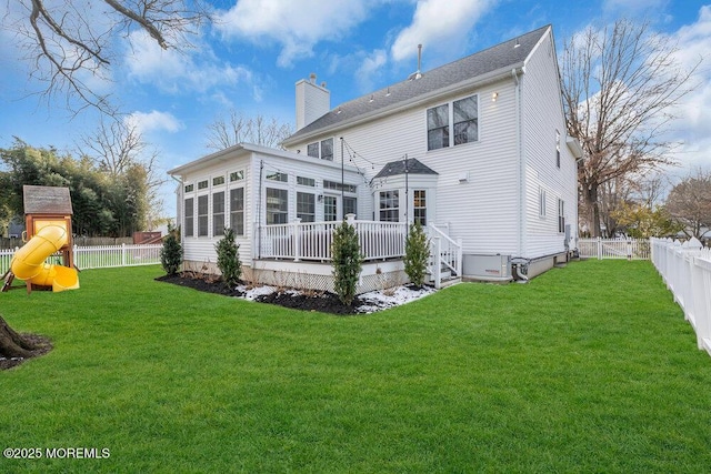 back of house featuring a wooden deck, a playground, a sunroom, and a lawn