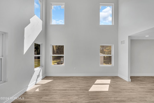 unfurnished living room featuring plenty of natural light, a high ceiling, and light wood-type flooring