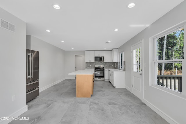 kitchen featuring backsplash, stainless steel appliances, sink, white cabinets, and a center island