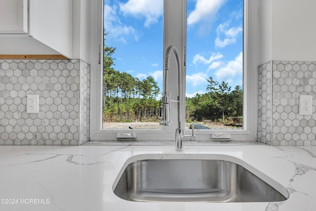 room details with white cabinets, sink, light stone counters, and backsplash