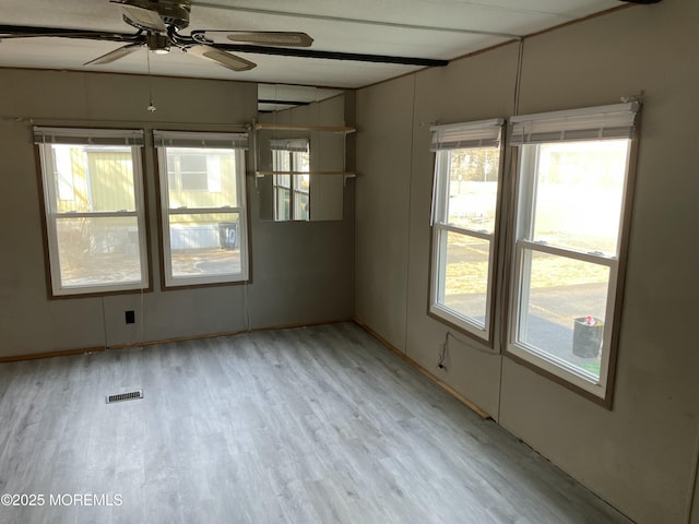 spare room with a ceiling fan, a wealth of natural light, visible vents, and wood finished floors