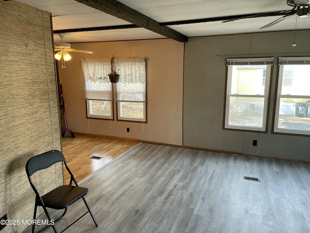 empty room featuring ceiling fan, beam ceiling, wood finished floors, and visible vents