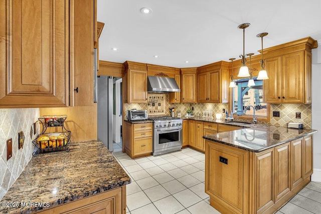 kitchen featuring dark stone counters, wall chimney range hood, sink, hanging light fixtures, and high end stove