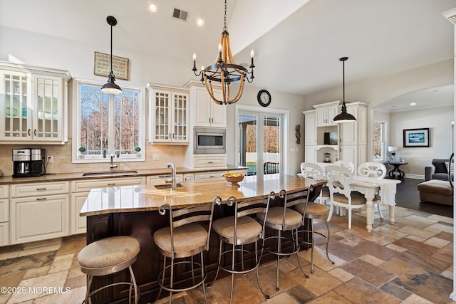 kitchen featuring stainless steel microwave, backsplash, sink, light stone countertops, and an island with sink