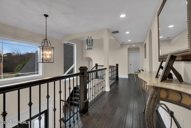 corridor with dark wood-type flooring and an inviting chandelier