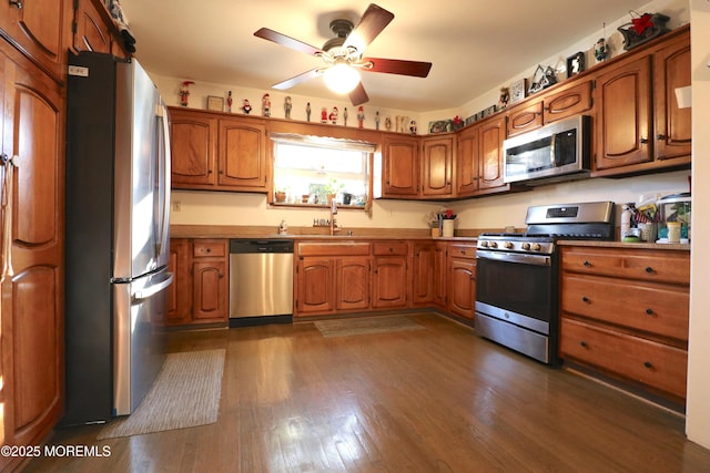 kitchen featuring stainless steel appliances, dark wood-style floors, ceiling fan, and brown cabinetry