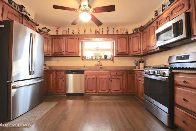 kitchen with dark wood-style floors, appliances with stainless steel finishes, brown cabinetry, and a sink