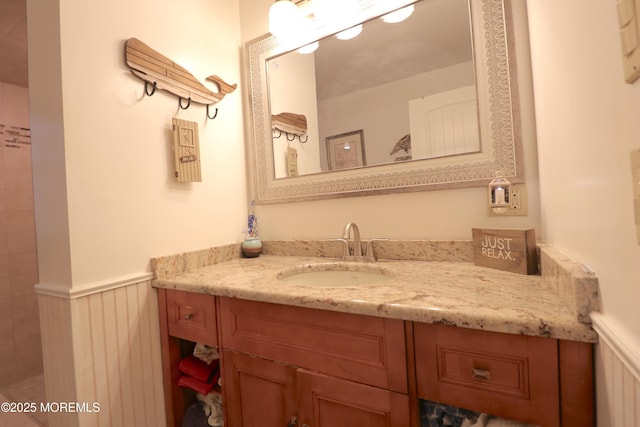 full bath with vanity, a tile shower, and wainscoting