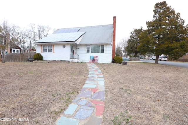 view of front of property featuring fence, roof mounted solar panels, and a chimney