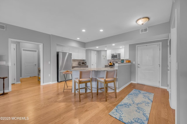 kitchen with white cabinetry, stainless steel appliances, light hardwood / wood-style flooring, kitchen peninsula, and a breakfast bar area