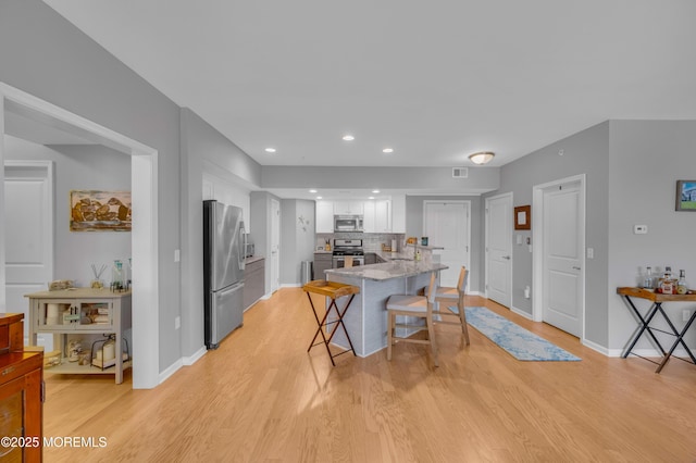 kitchen featuring a breakfast bar area, white cabinets, stainless steel appliances, and light wood-type flooring