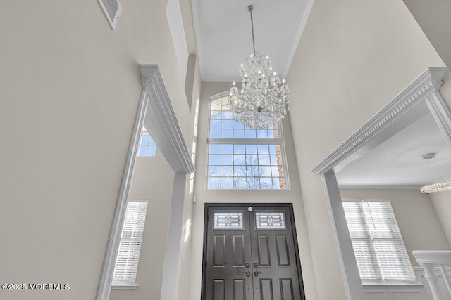 foyer entrance with a high ceiling, crown molding, and an inviting chandelier