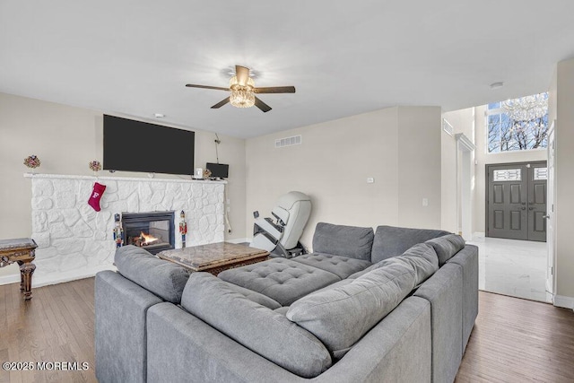 living room featuring hardwood / wood-style flooring, ceiling fan, and a stone fireplace