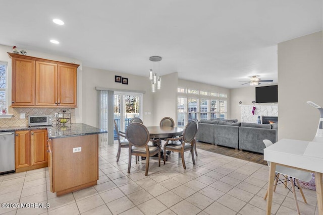 kitchen with decorative light fixtures, light tile patterned floors, stainless steel dishwasher, dark stone counters, and decorative backsplash