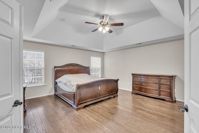 bedroom with wood-type flooring, ceiling fan, and a tray ceiling