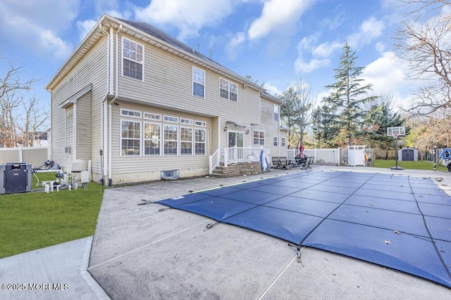 rear view of property with a covered pool, a yard, central air condition unit, and a patio area