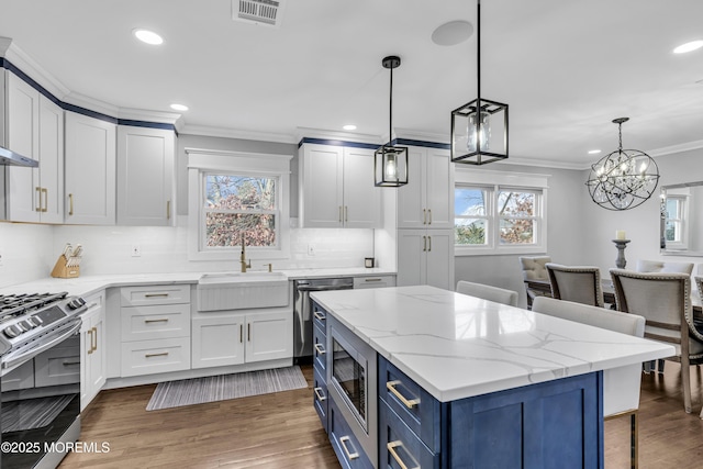 kitchen featuring visible vents, blue cabinetry, ornamental molding, a sink, and appliances with stainless steel finishes