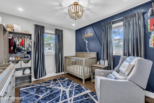 bedroom with a crib, a notable chandelier, wood finished floors, recessed lighting, and baseboards